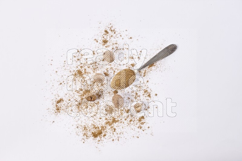 A metal spoon full of nutmeg powder with some of the powder and seeds beside it on a white flooring