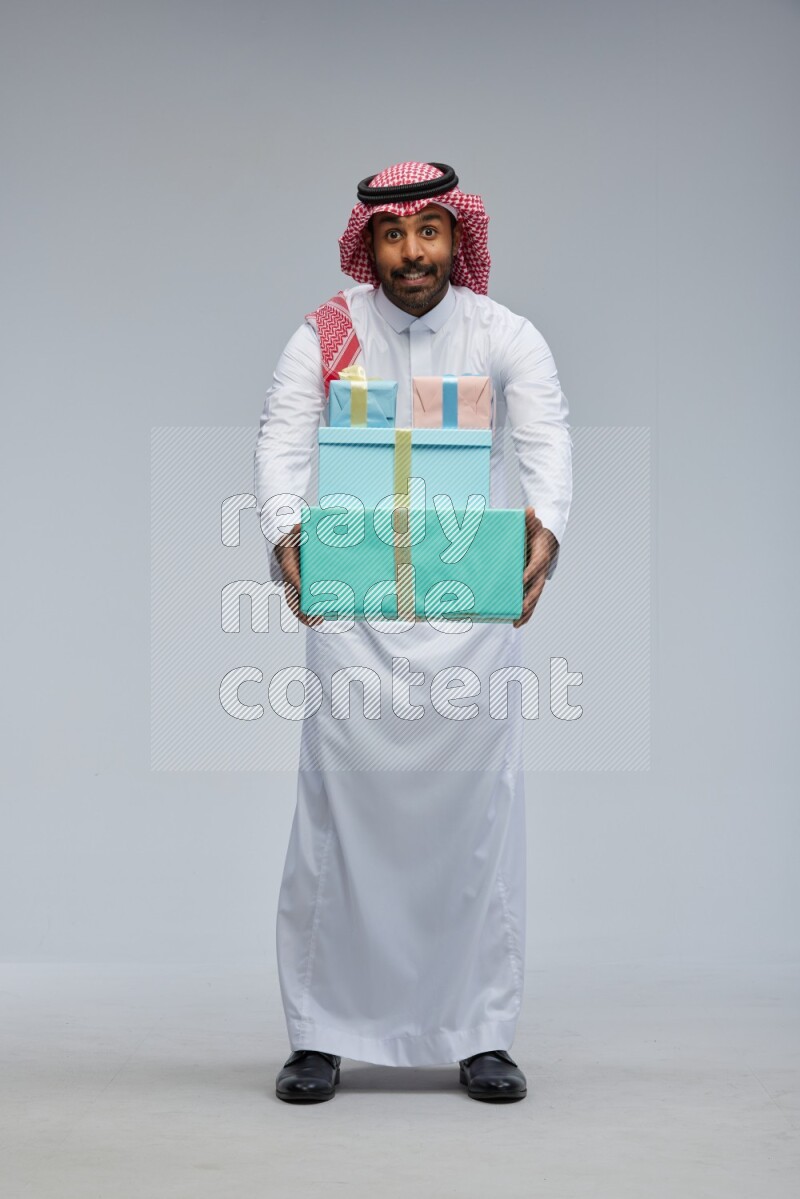 Saudi man Wearing Thob and shomag standing holding gift box on Gray background