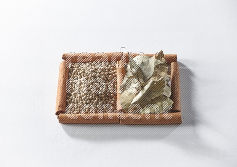 مربعان من أعواد القرفة ممتلئان بحبوب الفلفل الأبيض وأوراق الغار علي خلفية بيضاء