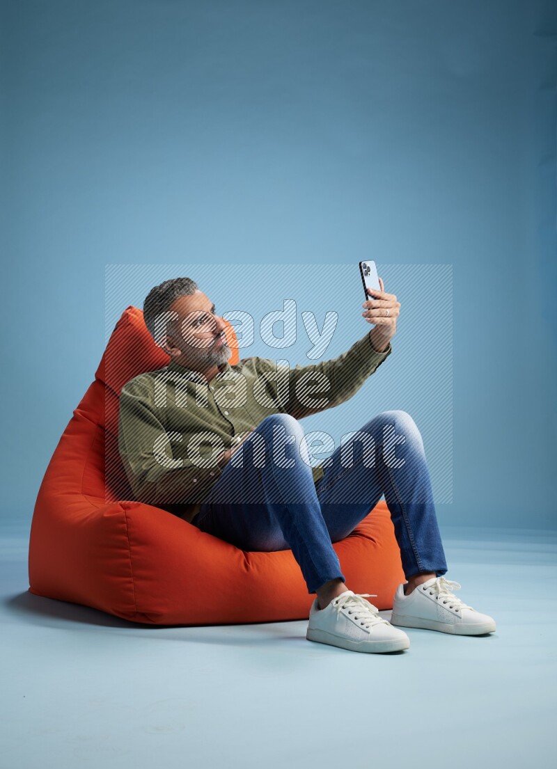 A man sitting on an orange beanbag and taking selfie