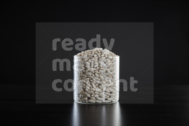 White beans in a glass jar on black background