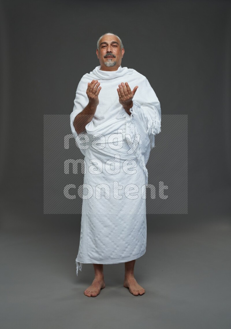A man wearing Ehram Standing dua'a on gray background