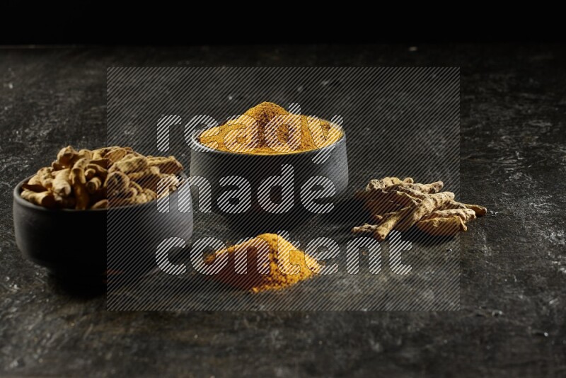 وعاءان من الفخار باللون الأسود، أحدهما ممتلئ ببودرة الكركم والآخر ممتلئ بأصابع كاملة من الكركم المجفف على خلفية سوداء