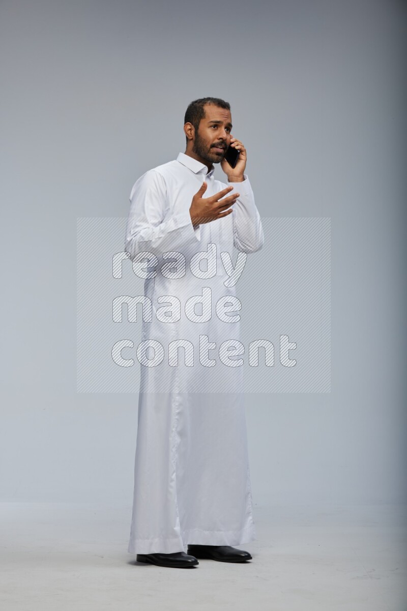Saudi man wearing Thob standing talking on phone on Gray background