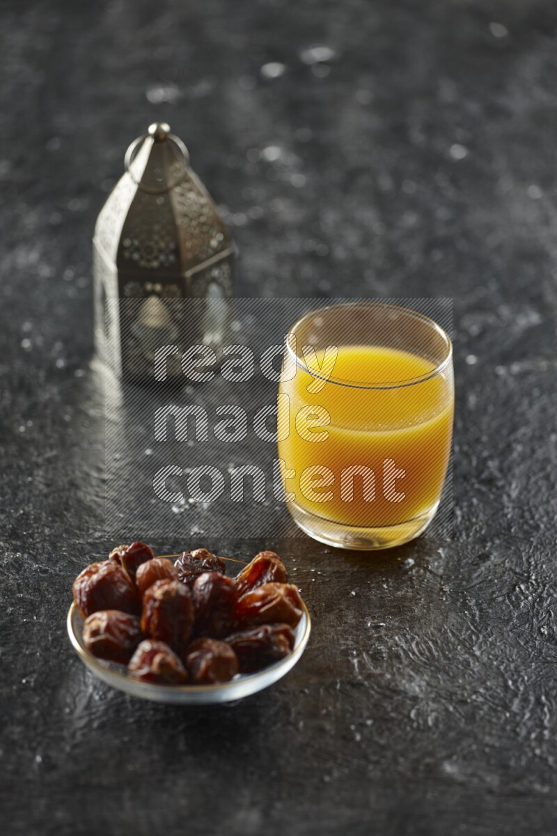 A silver lantern with different drinks, dates, nuts, prayer beads and quran on textured black background