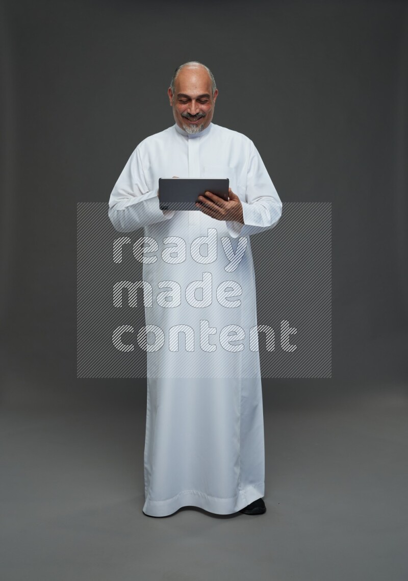 Saudi man without shomag Standing working on tablet on gray background
