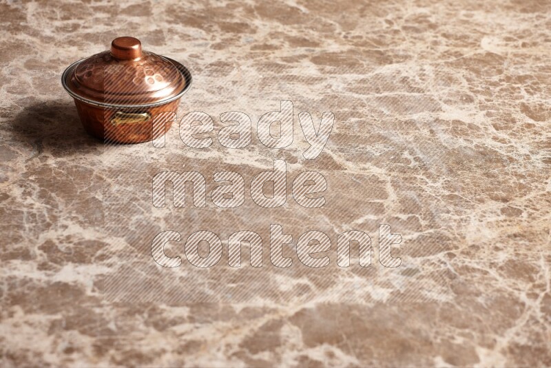 A small copper pot on beige marble background