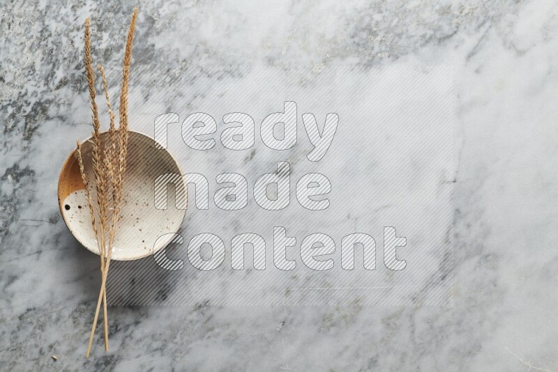 Wheat stalks on multicolored pottery plate on grey marble background