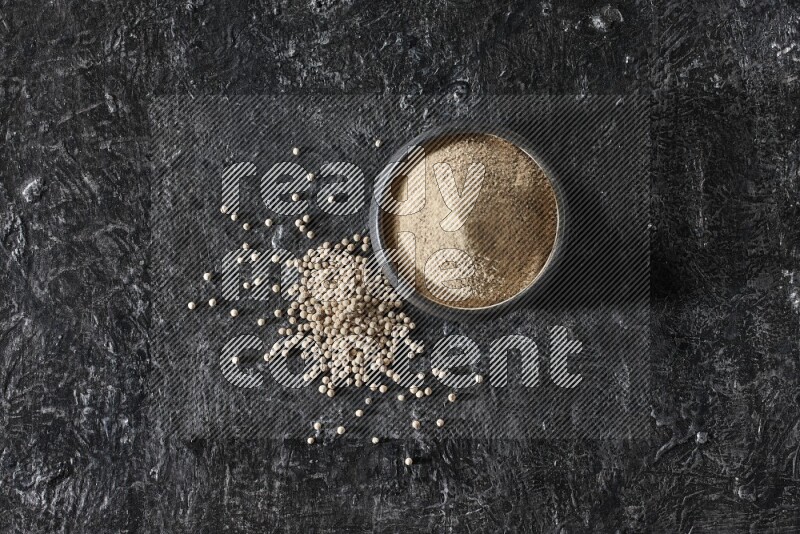 وعاء فخار أسود مملوء ببودرة الفلفل الأبيض مع حبات الفلفل الأبيض على أرضية سوداء