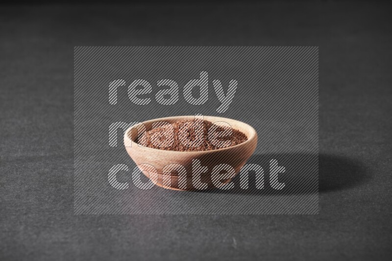 A wooden bowl full of garden cress seeds on a black flooring