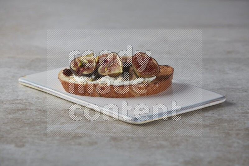figs halves with cream cheese on toasted sourdough slice on a wooden board on textured grey background