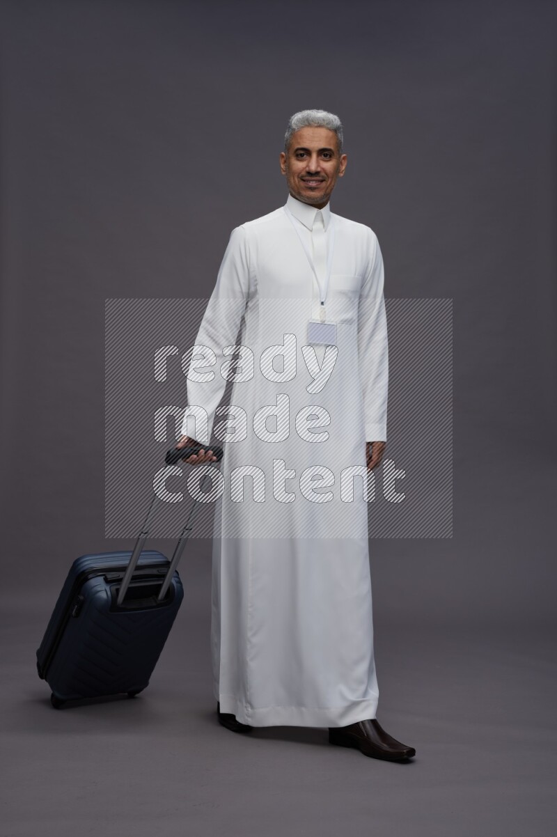 Saudi man wearing thob with neck strap employee badge standing holding bag on gray background