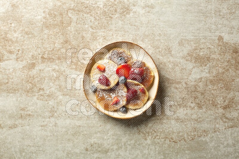 Five stacked mixed berries mini pancakes in an irregular plate on beige background