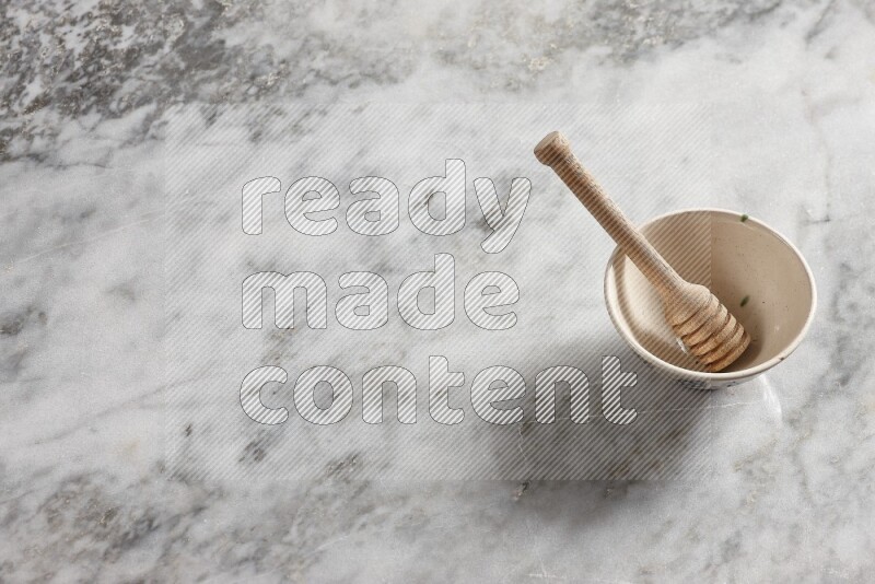 Beige pottery bowl with wooden honey dipper in it on grey marble background