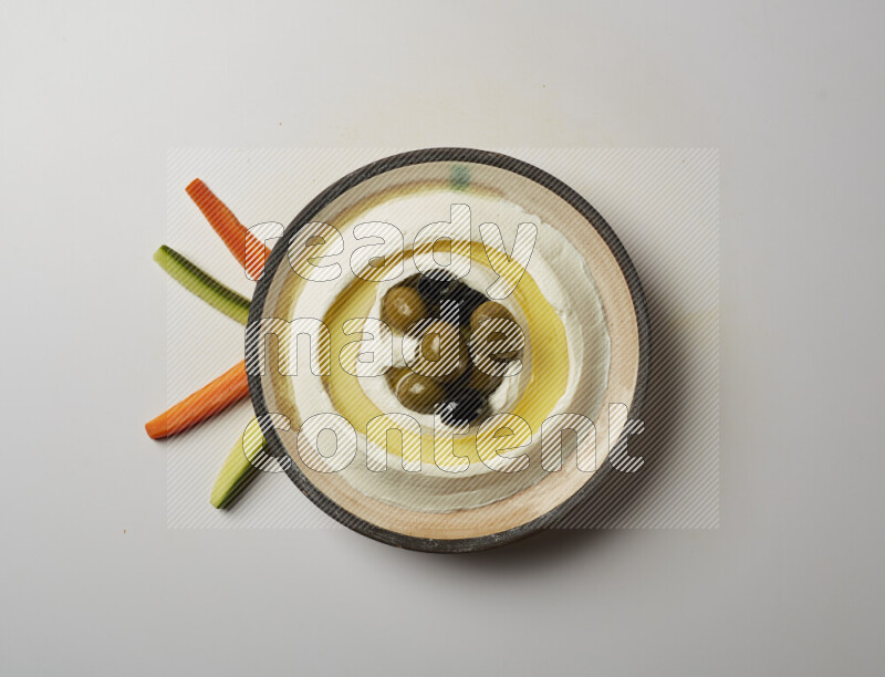 Lebnah garnished with whole black olives in a pottery plate on a white background