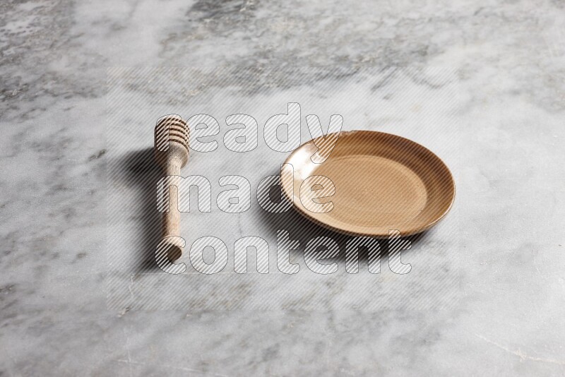Beige pottery plate with wooden honey dipper on the side on grey marble background