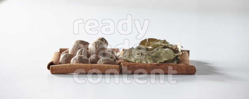 مربعان من أعواد القرفة ممتلئان بأوراق الغار وجوزة الطيب علي خلفية بيضاء