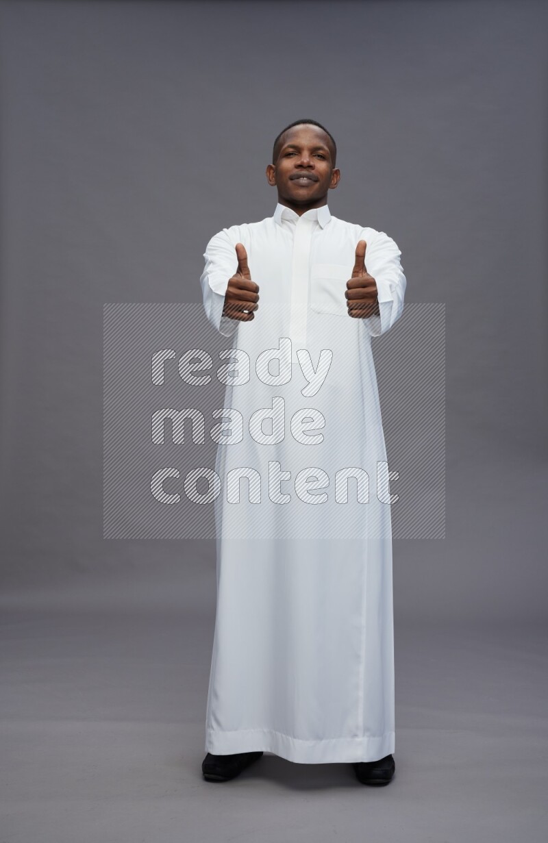 Saudi man wearing thob standing interacting with the camera on gray background