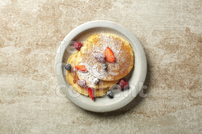 Three stacked mixed berries pancakes in a grey plate on beige background