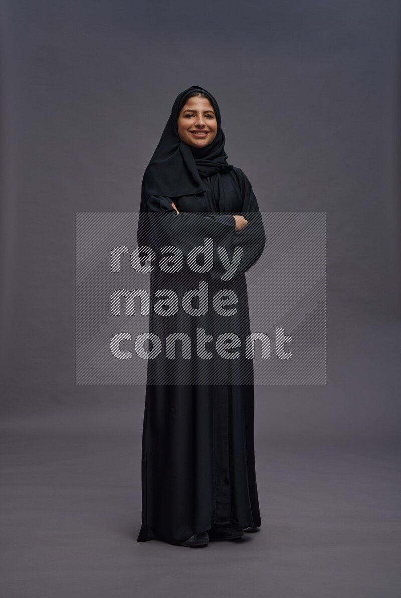 Saudi woman wearing Abaya standing with crossed arms on gray background
