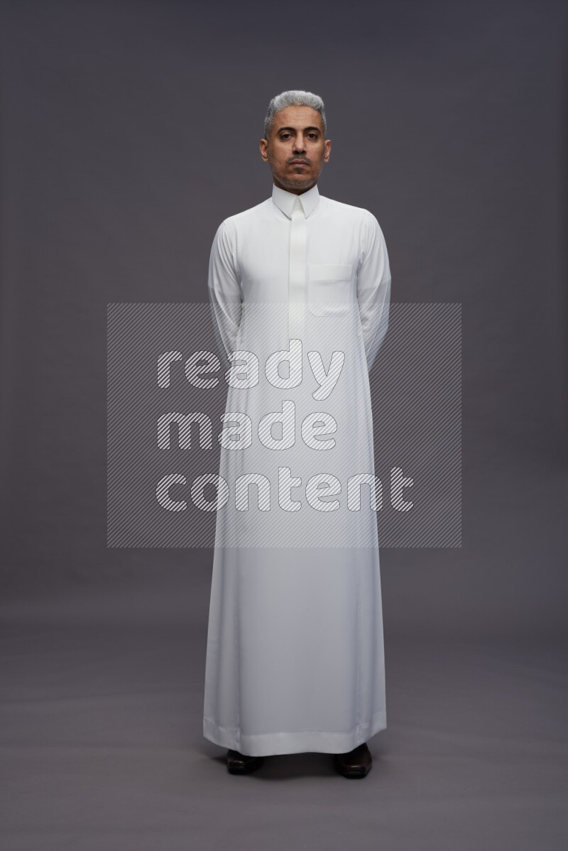 Saudi man wearing thob standing interacting with the camera on gray background
