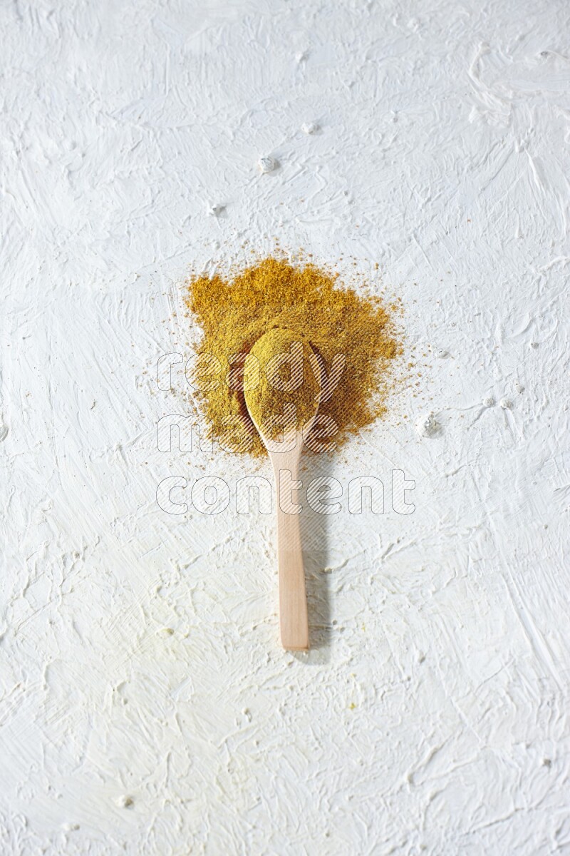 A wooden spoon full of turmeric powder on textured white background