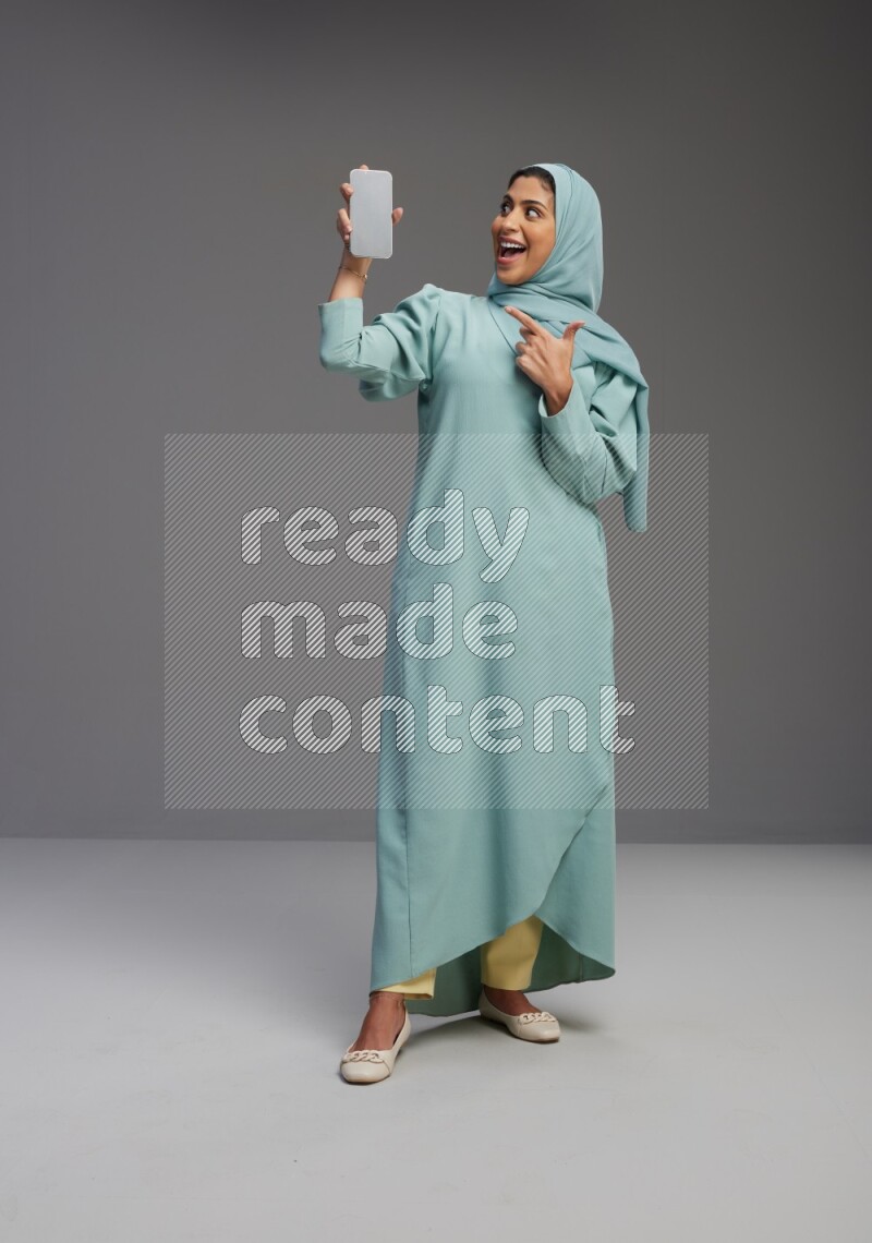 Saudi Woman wearing Abaya standing showing phone to camera on Gray background