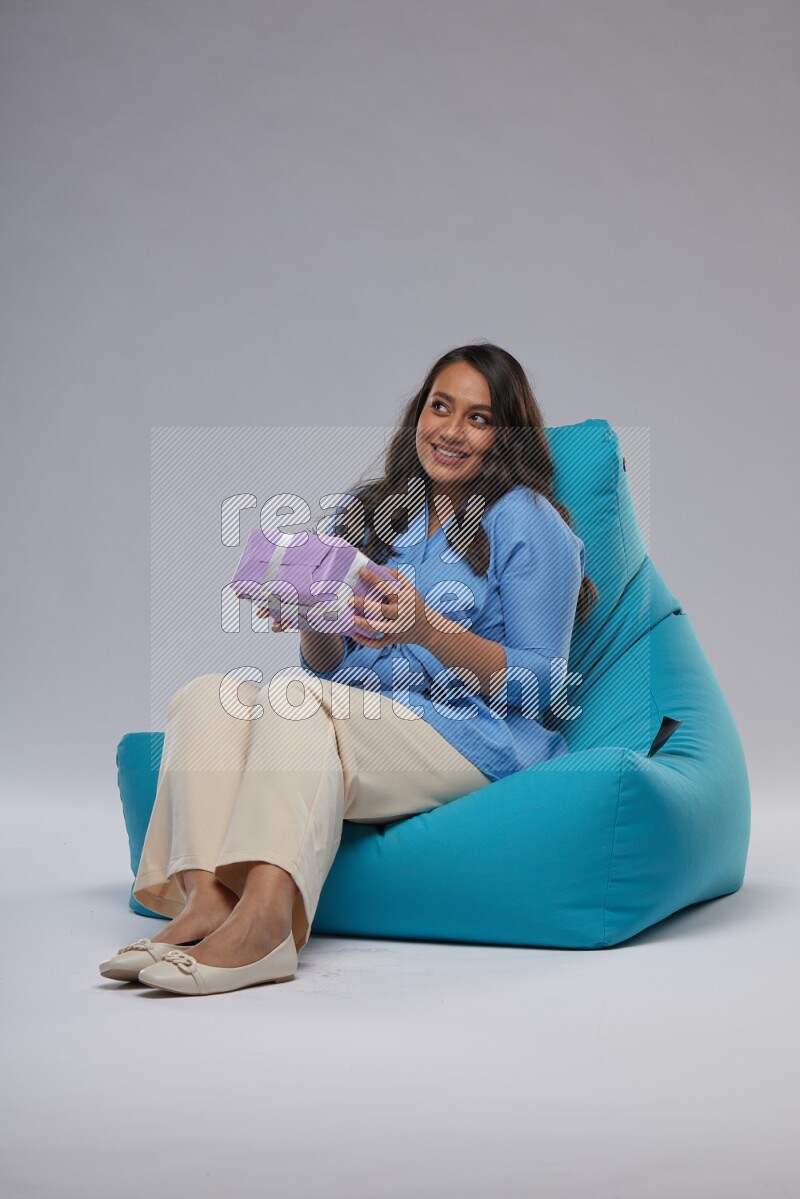 A woman sitting on a blue beanbag and holding a gift