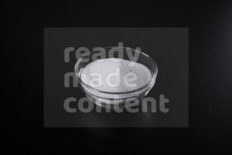 A glass bowl full of fine table salt on black background