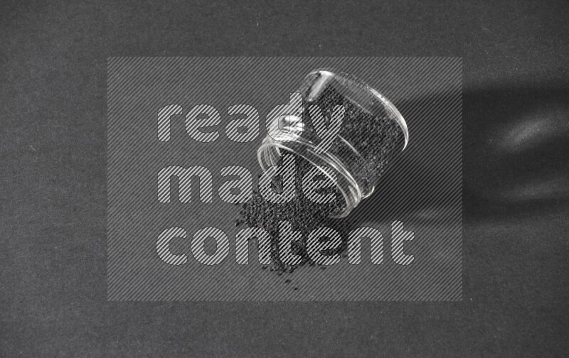 A flipped glass jar full of black seeds and the seeds spread out on a black flooring