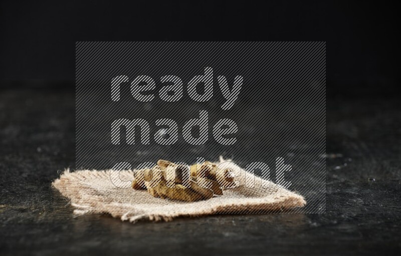 أصابع الكركم المجففة على قطعة من قماش الخيش على خلفية سوداء