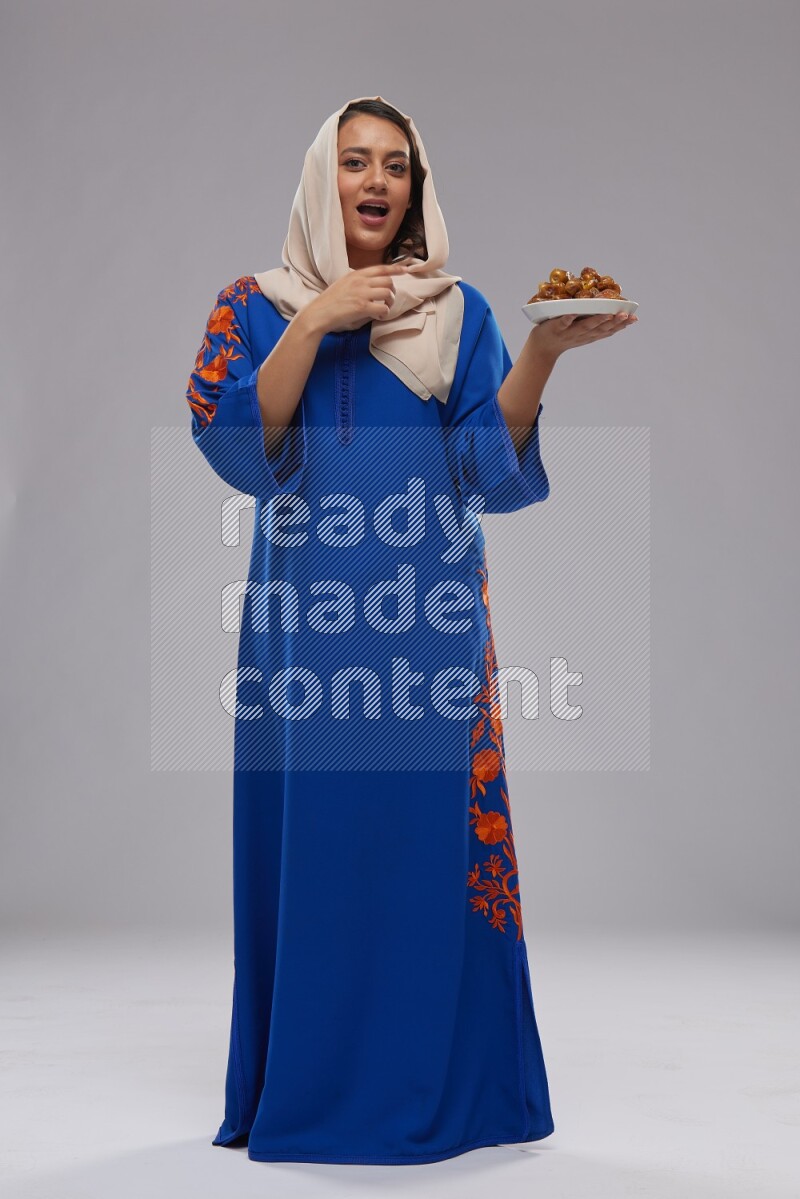 A Saudi woman standing wearing Jalabeya holding a plate of dates