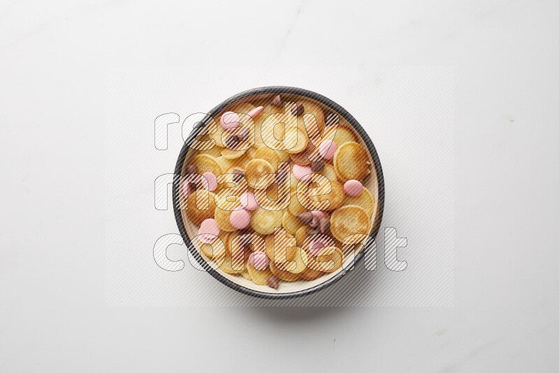 Top-view shot of mixed chocolate chips cereal pancakes in a round bowl on white background