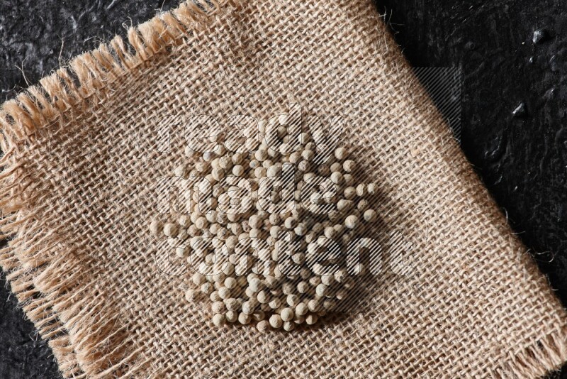 White pepper beads on a burlap piece of fabric on textured black flooring