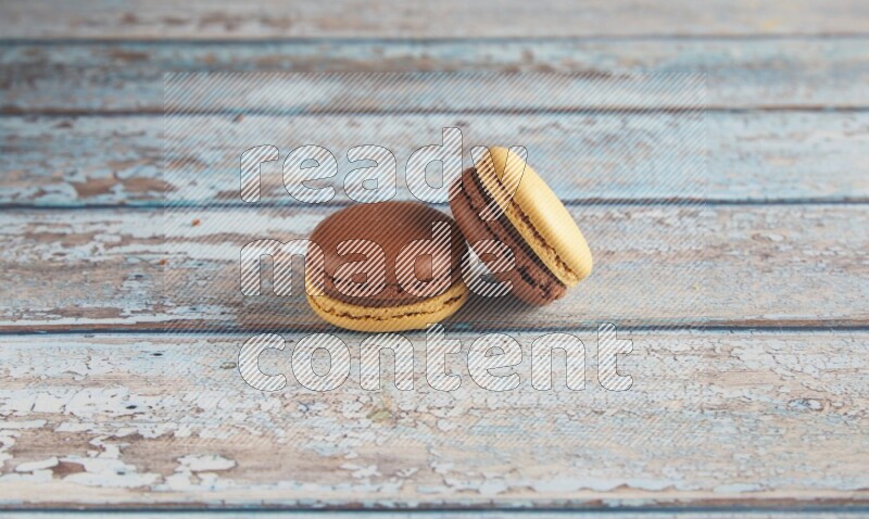 45º Shot of two Yellow and Brown Chai Latte macarons on light blue wooden background