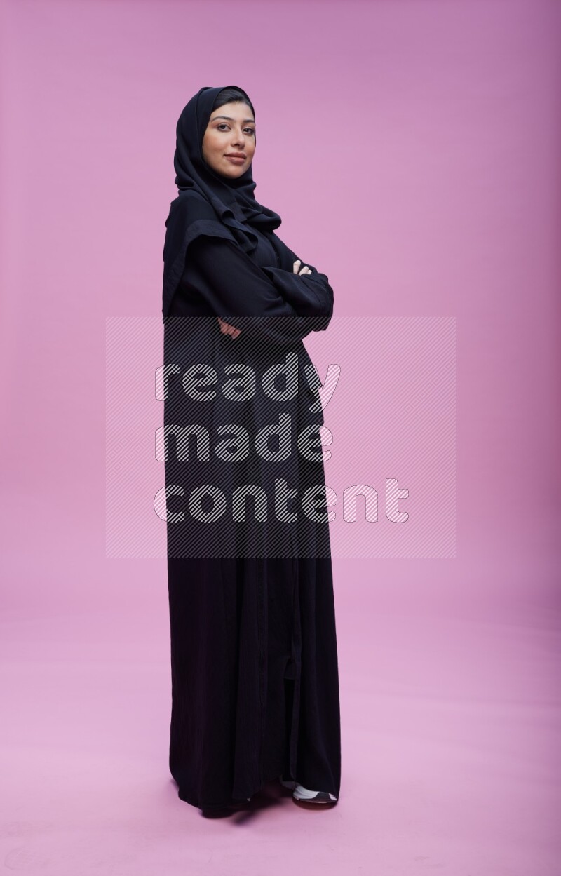 Saudi woman wearing Abaya standing with crossed arms on pink background