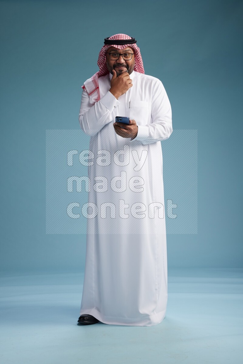 Saudi Man with shimag Standing texting on phone on blue background