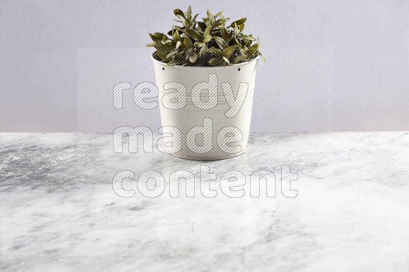 Green artificial plant in white pot on light grey marble background