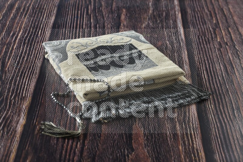 A folded prayer mat with different elements such as quran and prayer beads on brown wooden background