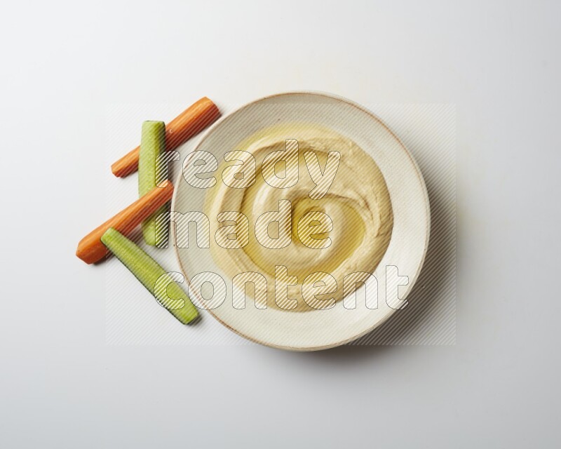 Hummus in a pottry plate garnished with olive oil on a white background