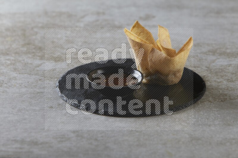 wonton cups with soy sauce ramkin on circle slate on grey textured counter top