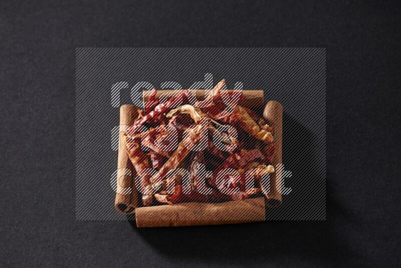 A single square of cinnamon sticks full of chilis on black flooring
