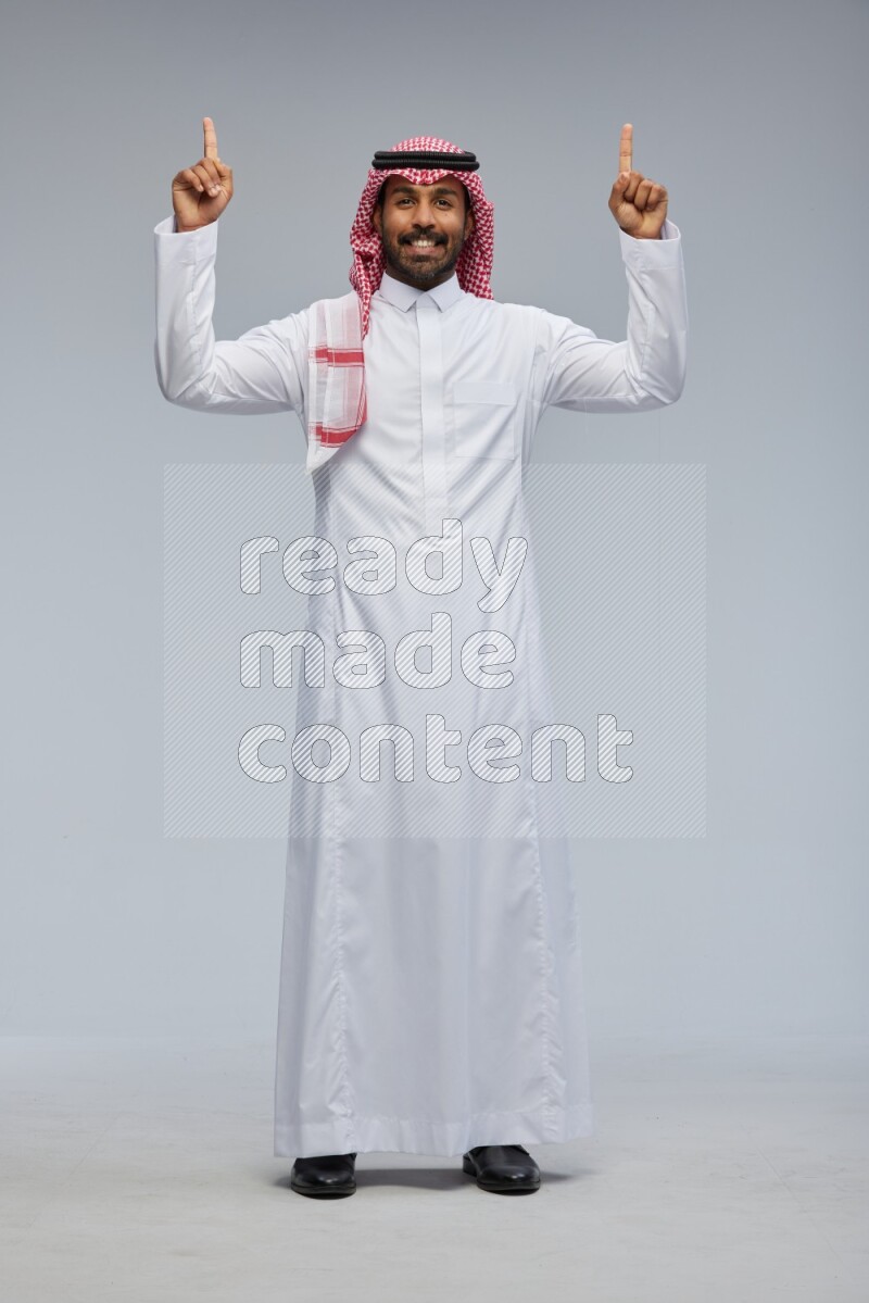 Saudi man Wearing Thob and shomag standing interacting with the camera on Gray background