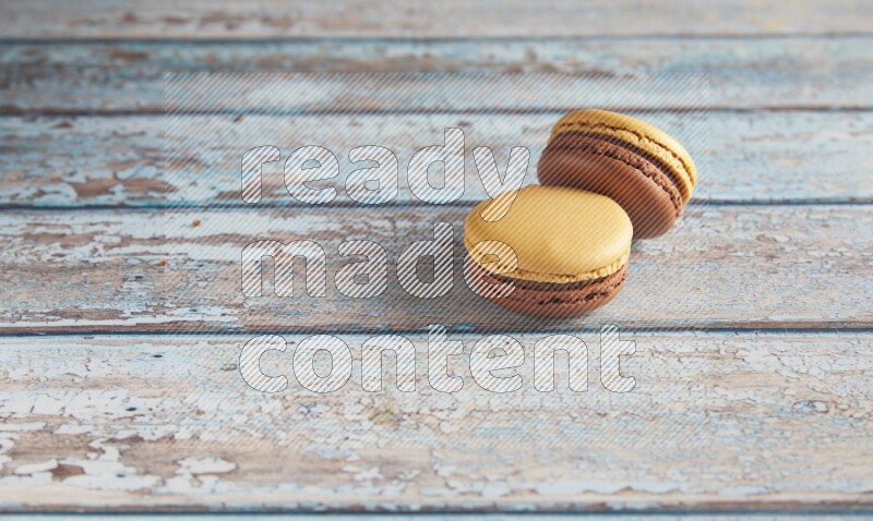 45º Shot of two Yellow and Brown Chai Latte macarons on light blue wooden background