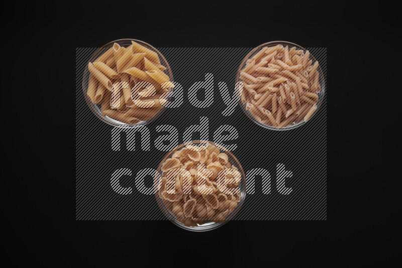 Different pasta types in glass bowls on black background