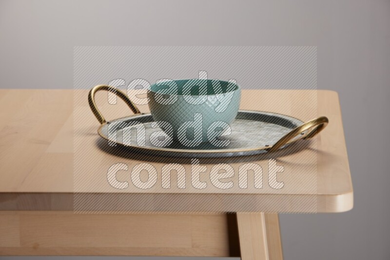 blue bowl placed on a rounded stainless steel metal tray with golden handels on the edge of wooden table