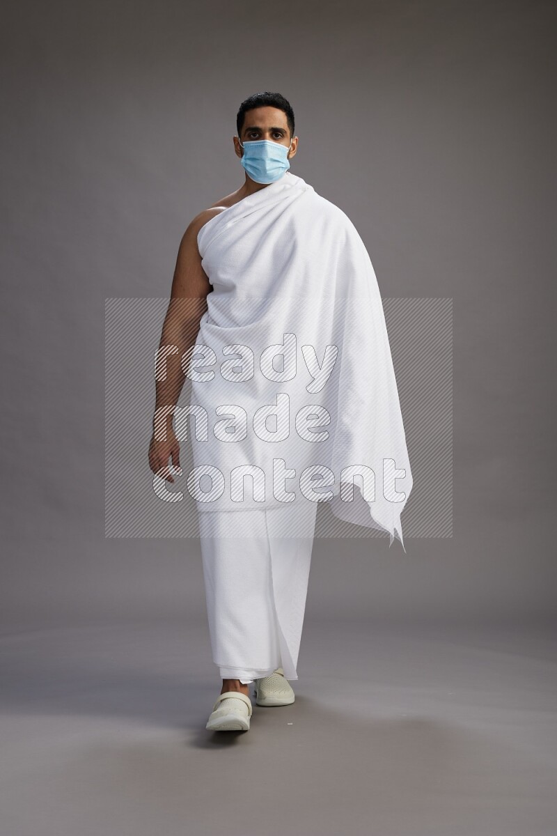 A man wearing Ehram with face mask Standing Interacting with the camera on gray background