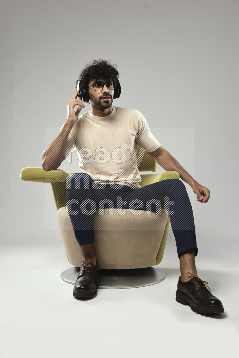A man wearing casual sitting on a chair putting on headphones on white background