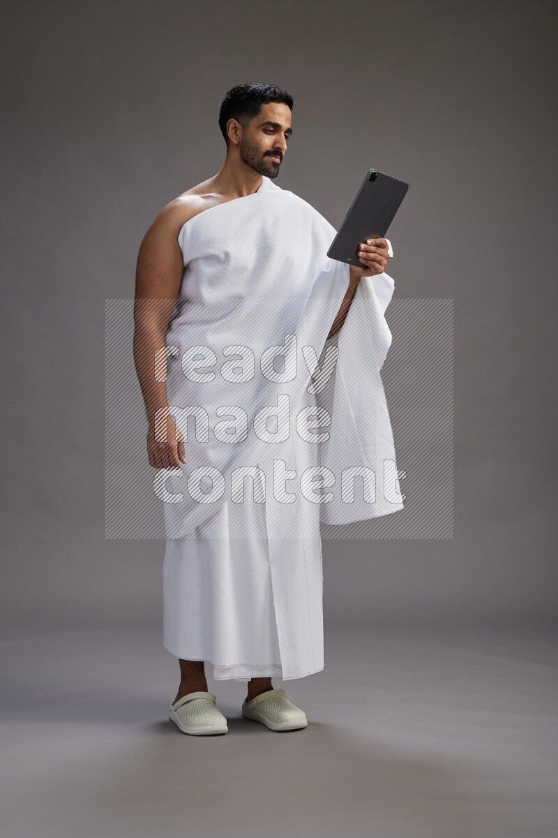 A man wearing Ehram and holding a tablet on gray background