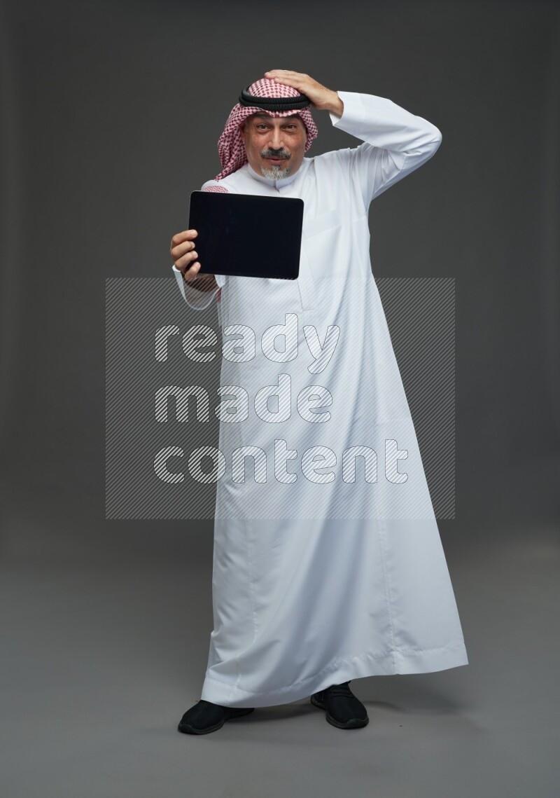 Saudi man with shomag Standing working on tablet on gray background